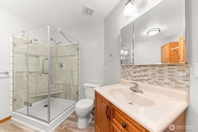 bathroom featuring toilet, visible vents, backsplash, and a stall shower