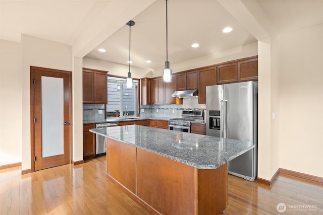 kitchen with under cabinet range hood, backsplash, a center island, appliances with stainless steel finishes, and light wood finished floors