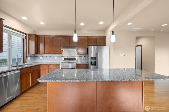 kitchen featuring a sink, light wood-style floors, under cabinet range hood, appliances with stainless steel finishes, and backsplash