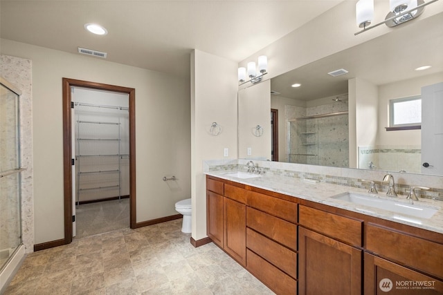 full bath featuring visible vents, double vanity, a sink, a shower stall, and a walk in closet