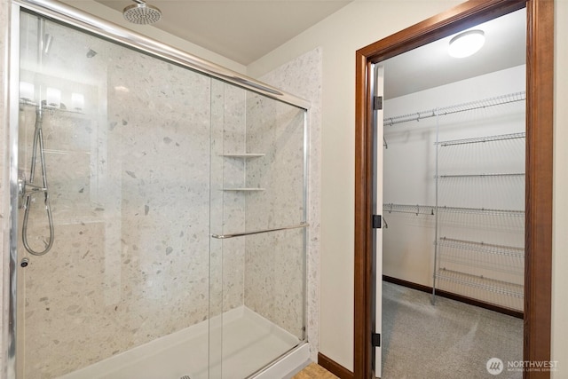 bathroom with baseboards, a spacious closet, and a shower stall