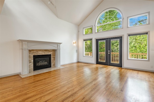 unfurnished living room with high vaulted ceiling, hardwood / wood-style floors, french doors, baseboards, and a tile fireplace