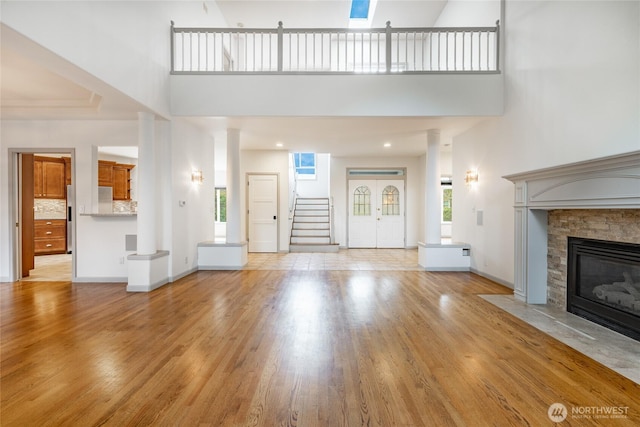 unfurnished living room with stairway, a high ceiling, a fireplace, and light wood finished floors