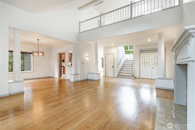 unfurnished living room with baseboards, stairway, light wood-type flooring, decorative columns, and a high ceiling