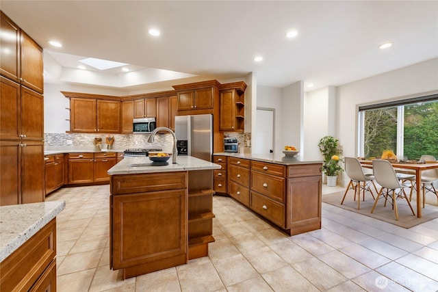 kitchen featuring open shelves, a kitchen island, brown cabinets, stainless steel appliances, and a sink