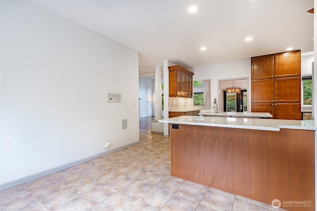kitchen featuring tasteful backsplash, recessed lighting, brown cabinetry, and light stone counters