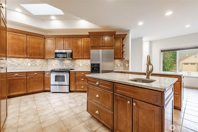 kitchen featuring a skylight, a sink, decorative backsplash, appliances with stainless steel finishes, and brown cabinets