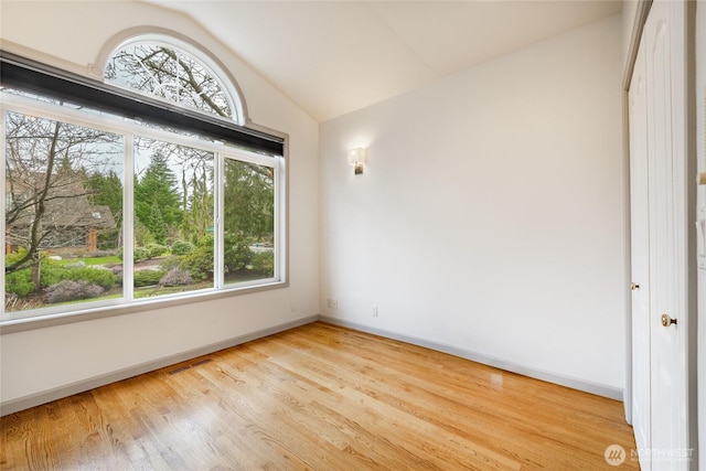 empty room featuring visible vents, lofted ceiling, baseboards, and wood finished floors