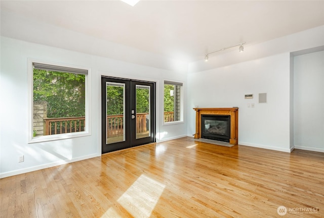 unfurnished living room featuring a fireplace with flush hearth, wood finished floors, baseboards, and french doors