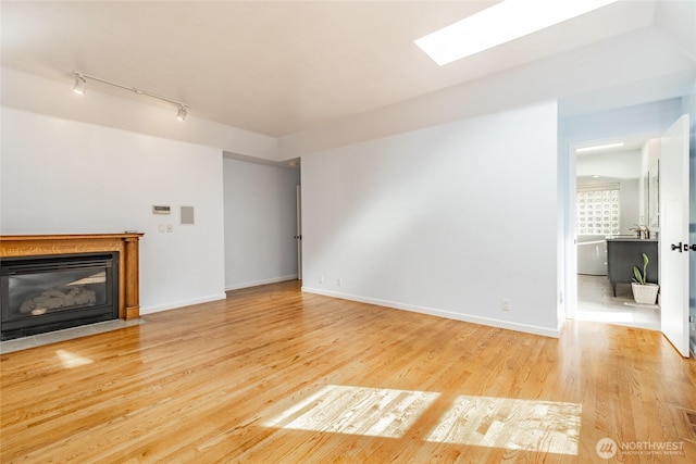 unfurnished living room with track lighting, a fireplace with flush hearth, wood finished floors, and baseboards