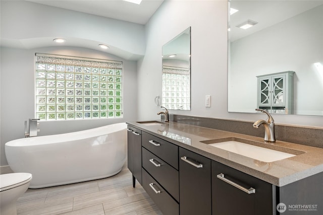 full bath with double vanity, a soaking tub, toilet, and a sink