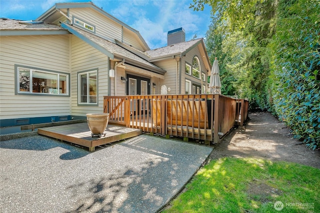 back of house featuring a shingled roof, a chimney, and a wooden deck