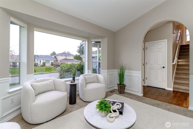 sitting room featuring stairway, a wainscoted wall, vaulted ceiling, carpet flooring, and arched walkways