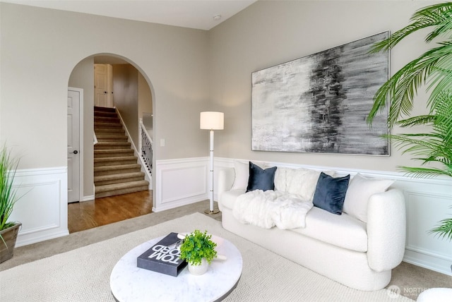 living area featuring arched walkways, carpet flooring, wainscoting, and stairs