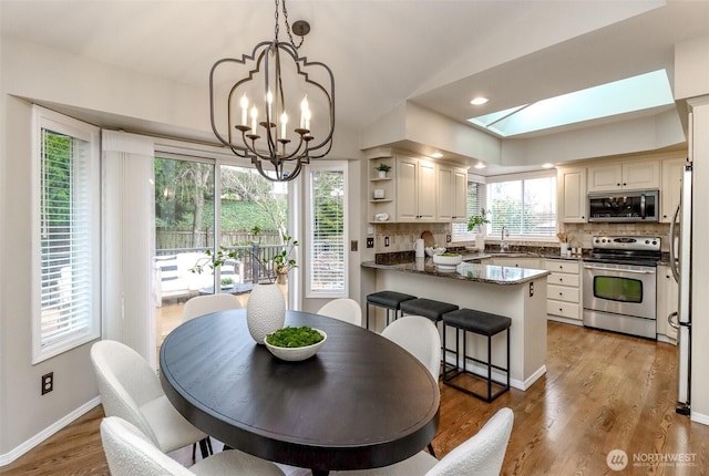 dining space with light wood-style flooring, recessed lighting, a skylight, baseboards, and a chandelier