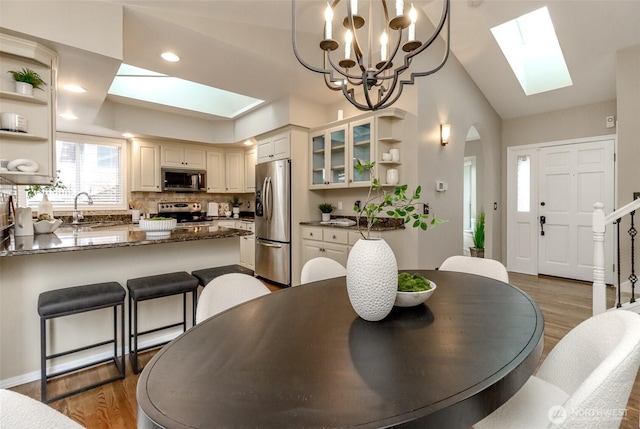 dining space featuring lofted ceiling with skylight, recessed lighting, wood finished floors, and arched walkways