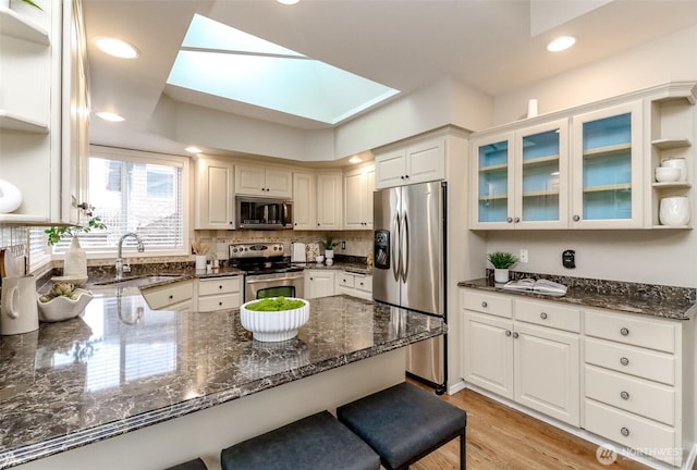 kitchen with a sink, dark stone counters, appliances with stainless steel finishes, and a peninsula