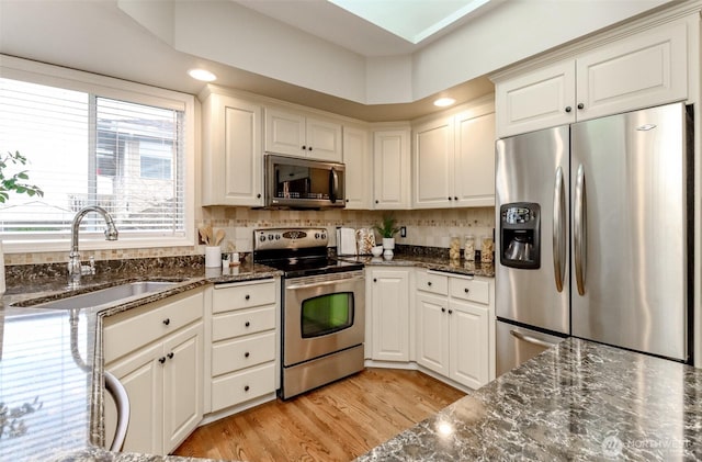 kitchen with light wood finished floors, tasteful backsplash, dark stone counters, appliances with stainless steel finishes, and a sink