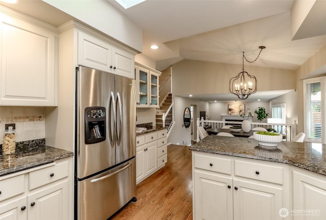 kitchen featuring light wood finished floors, decorative backsplash, stainless steel fridge, and dark stone countertops