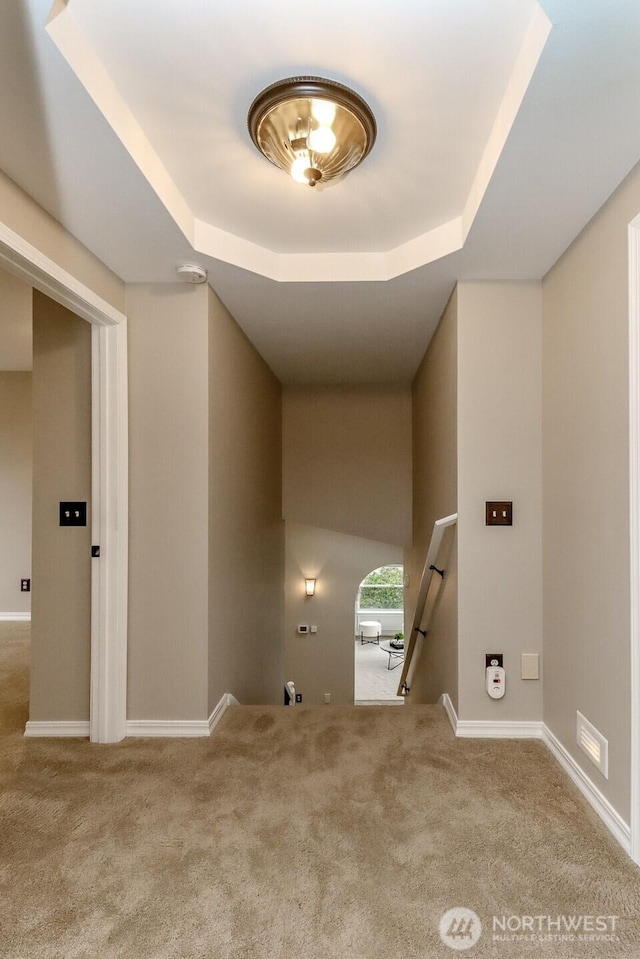 interior space with an upstairs landing, carpet flooring, baseboards, and a tray ceiling