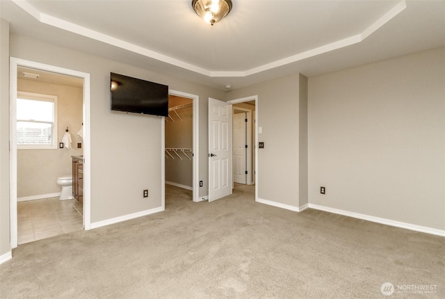 unfurnished bedroom featuring a raised ceiling, connected bathroom, carpet flooring, baseboards, and a spacious closet