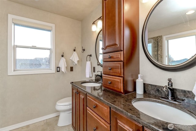 bathroom featuring a sink, baseboards, toilet, and double vanity