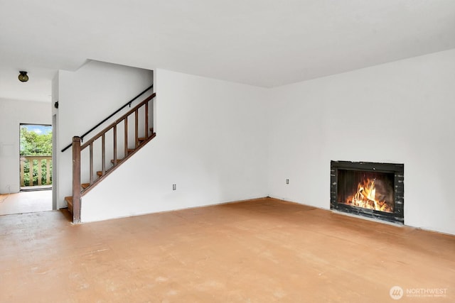 unfurnished living room featuring stairway and a lit fireplace