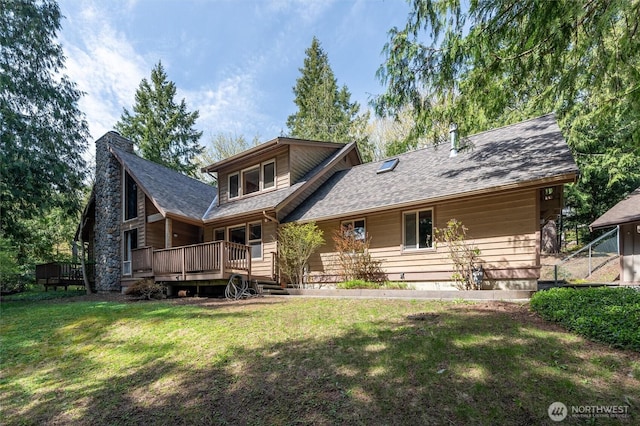 rear view of house featuring a wooden deck, a lawn, a chimney, and a shingled roof