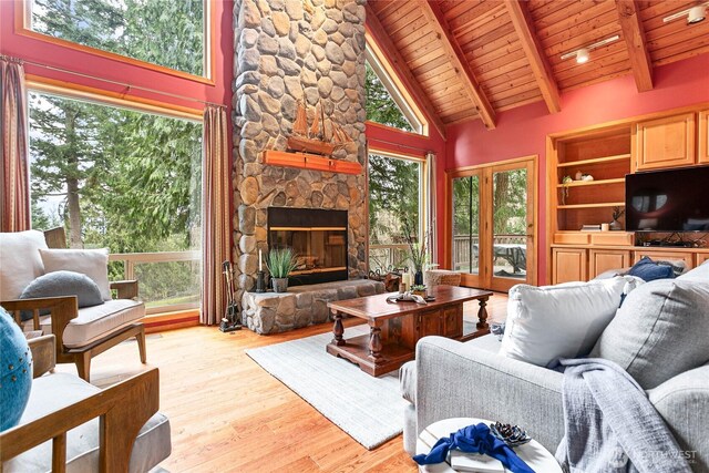 living room with a stone fireplace, light wood-style flooring, wood ceiling, and beamed ceiling