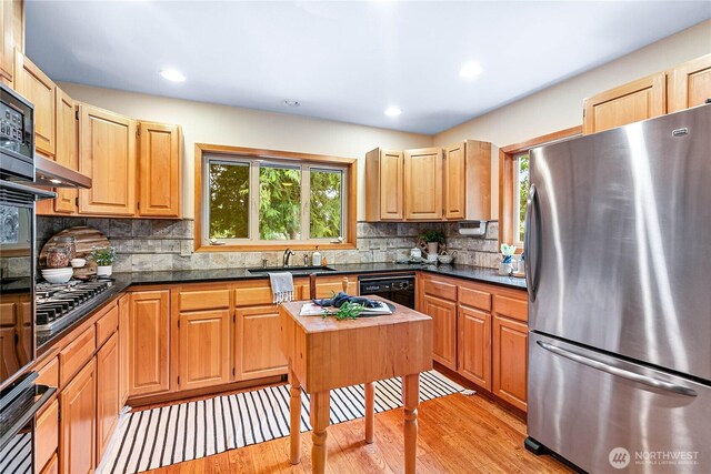 kitchen featuring light wood finished floors, tasteful backsplash, black dishwasher, freestanding refrigerator, and a sink