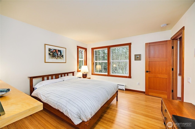 bedroom featuring light wood finished floors, a baseboard heating unit, and baseboards