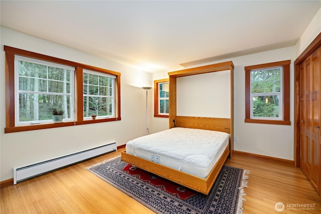 bedroom with a baseboard radiator, baseboards, light wood-style floors, and a closet