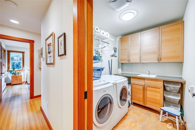 laundry room featuring baseboards, light wood-style floors, cabinet space, independent washer and dryer, and a sink