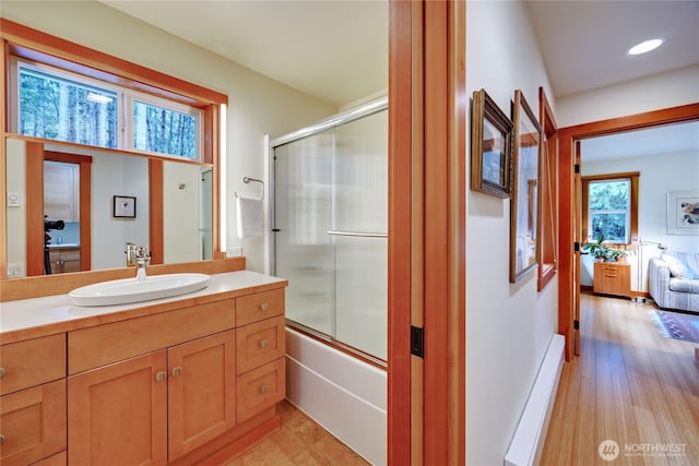 bathroom featuring vanity, baseboard heating, wood finished floors, enclosed tub / shower combo, and ensuite bath