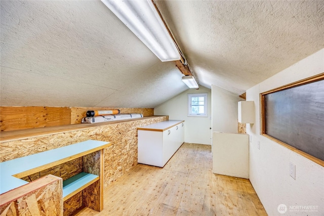 additional living space featuring light wood-type flooring, a textured ceiling, and vaulted ceiling