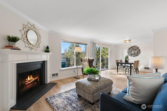 living room with light wood-type flooring, visible vents, ornamental molding, and a tiled fireplace