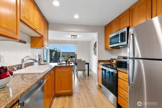 kitchen with a sink, appliances with stainless steel finishes, light wood-style flooring, and brown cabinetry