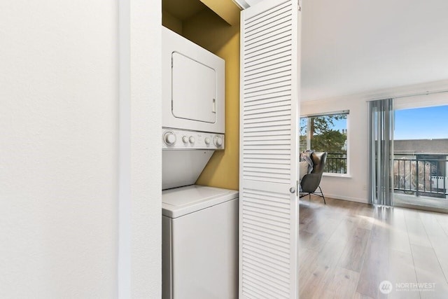 laundry room featuring laundry area, wood finished floors, baseboards, and stacked washing maching and dryer