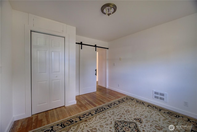 unfurnished bedroom with wood finished floors, visible vents, baseboards, a closet, and a barn door