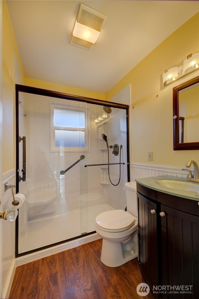 bathroom featuring wainscoting, toilet, a shower stall, and wood finished floors