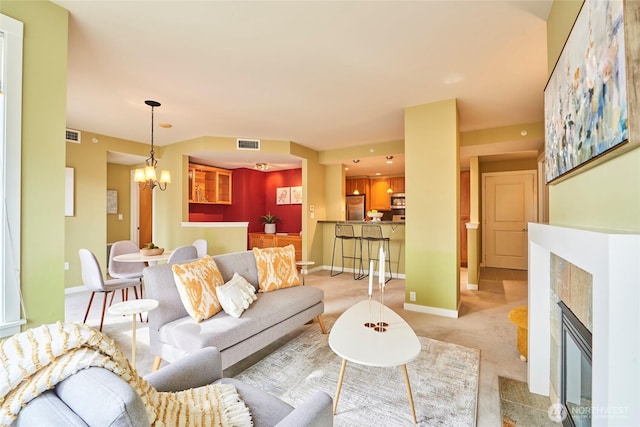 living area featuring visible vents, a notable chandelier, a tiled fireplace, baseboards, and light colored carpet