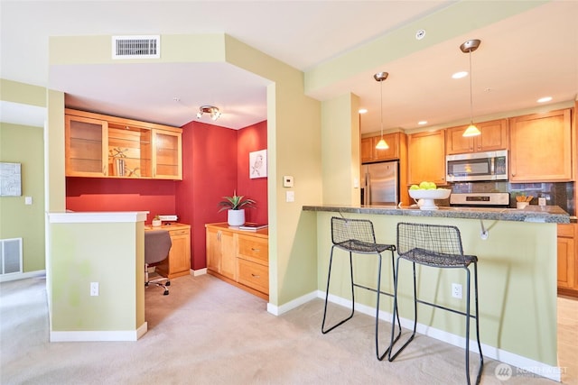 kitchen with baseboards, visible vents, appliances with stainless steel finishes, a kitchen breakfast bar, and light colored carpet