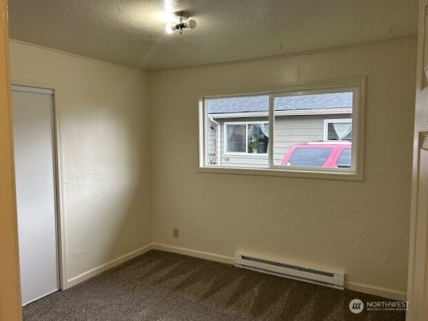 empty room featuring dark colored carpet, baseboards, baseboard heating, and a textured ceiling