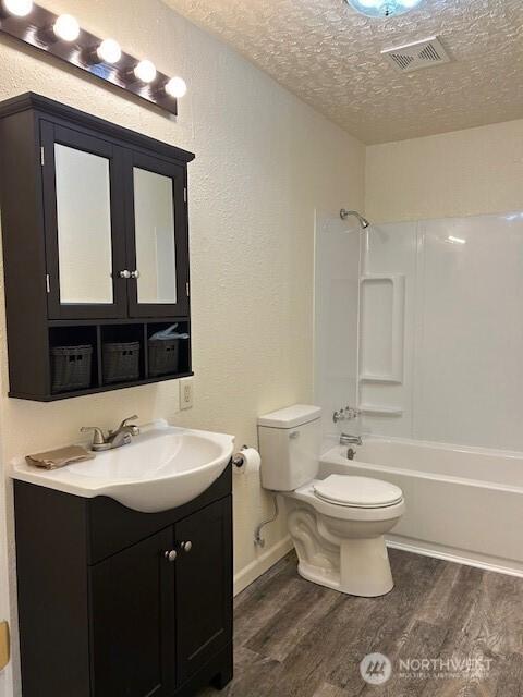 full bathroom with wood finished floors, visible vents, a textured ceiling, bathing tub / shower combination, and toilet