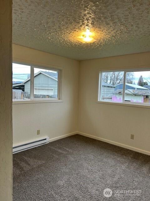 carpeted spare room featuring baseboards, baseboard heating, and a textured ceiling