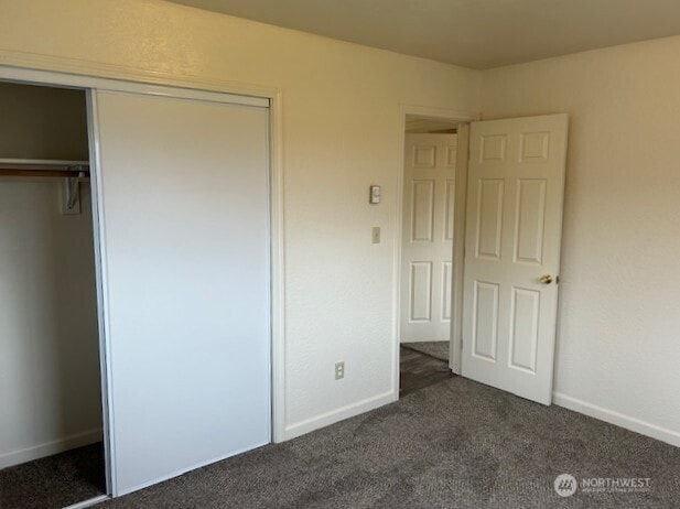 unfurnished bedroom featuring baseboards, dark colored carpet, and a closet