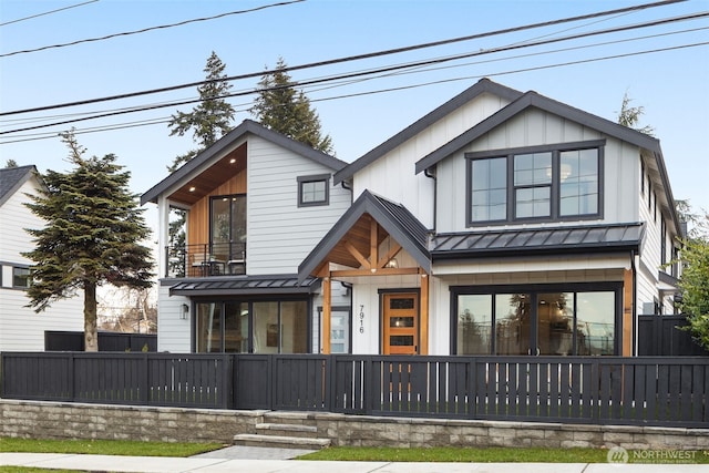 view of front of home featuring a balcony, fence, a standing seam roof, board and batten siding, and metal roof