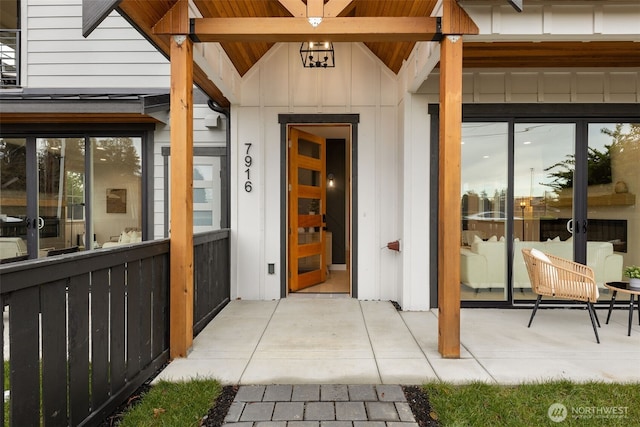 view of exterior entry with a patio, board and batten siding, and fence