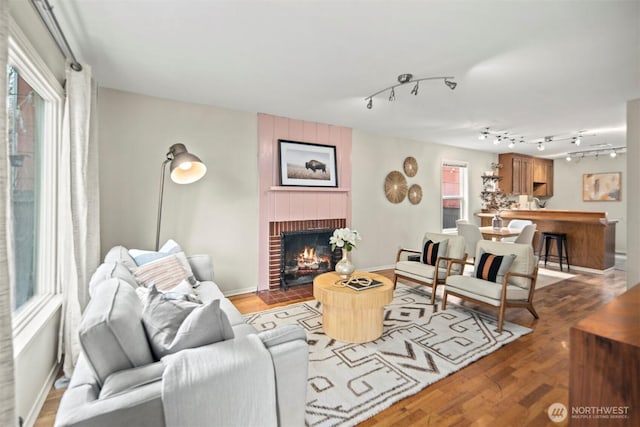 living room with a brick fireplace, rail lighting, baseboards, and wood finished floors