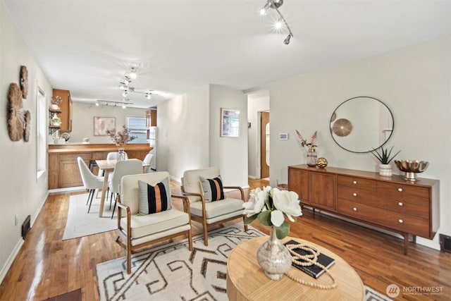 living area featuring track lighting, baseboards, and light wood-type flooring